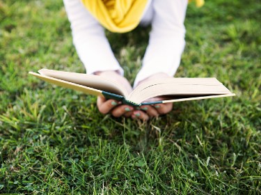 hands holding book in grass